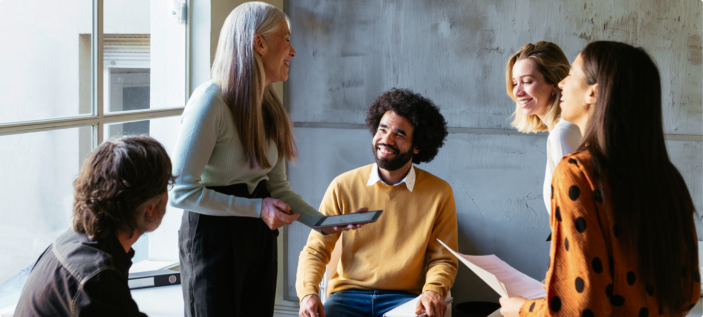 A group of five colleagues smiling and collaborating in a meeting room.